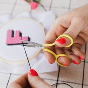 Person cutting thread with yellow scissors over an embroidery project.