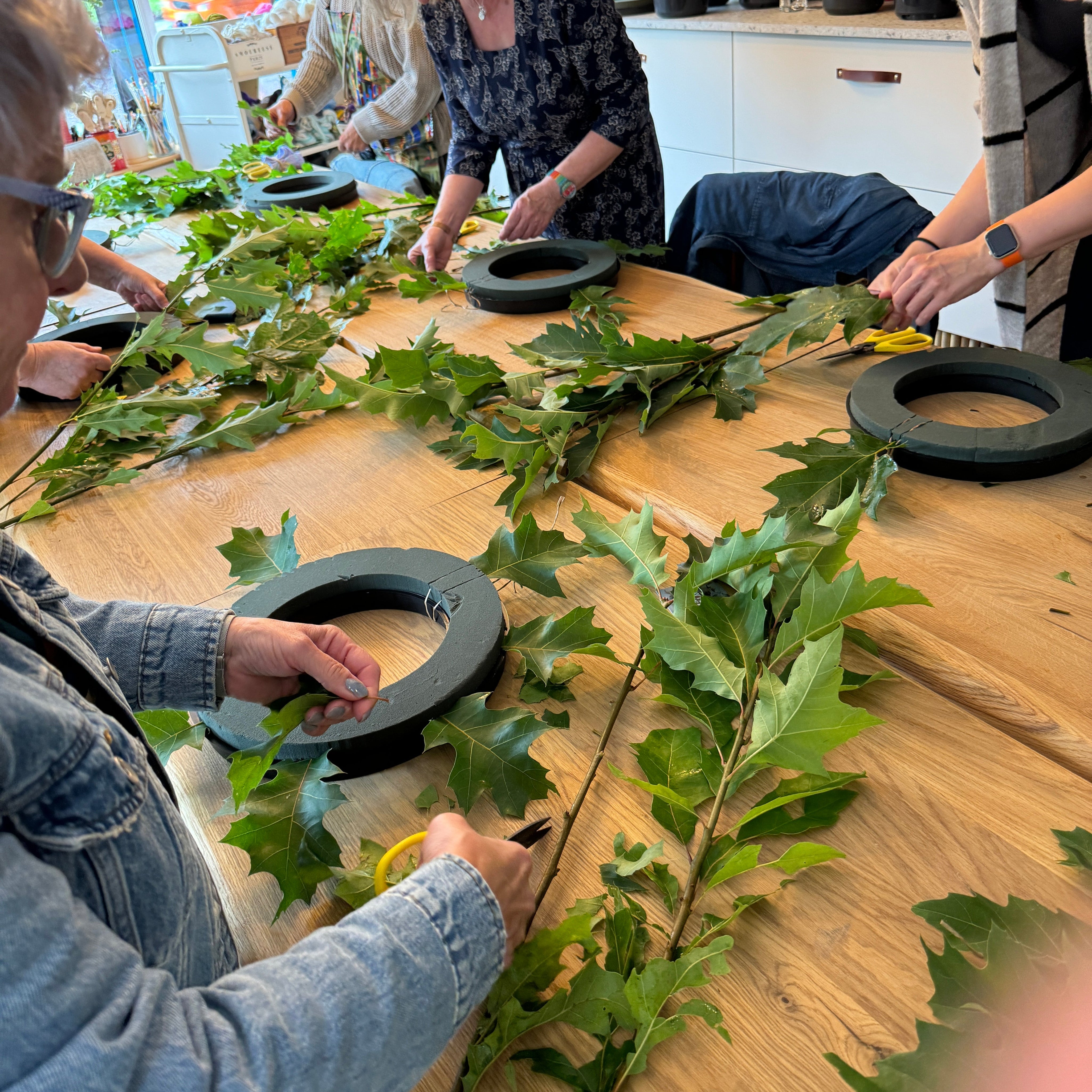 People arranging green leaves on a wooden surface with a blurred indoor background