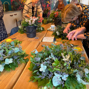 People working on floral arrangements at a table with a colorful floral backdrop.