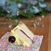 Slice of layered cake with cherry on a floral napkin on a wooden table with blurred background
