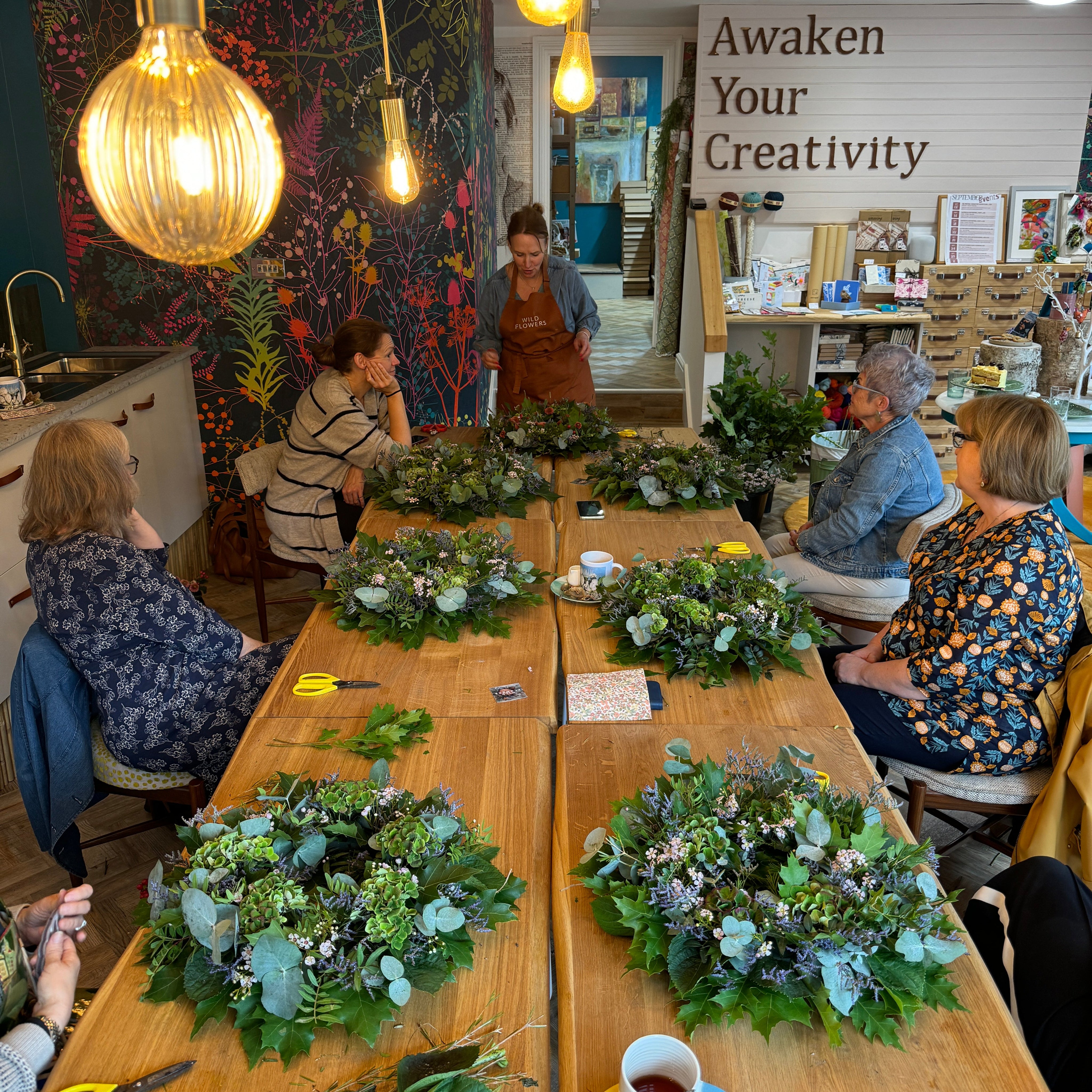 People working on wreaths in a room with decorative lights and furniture.