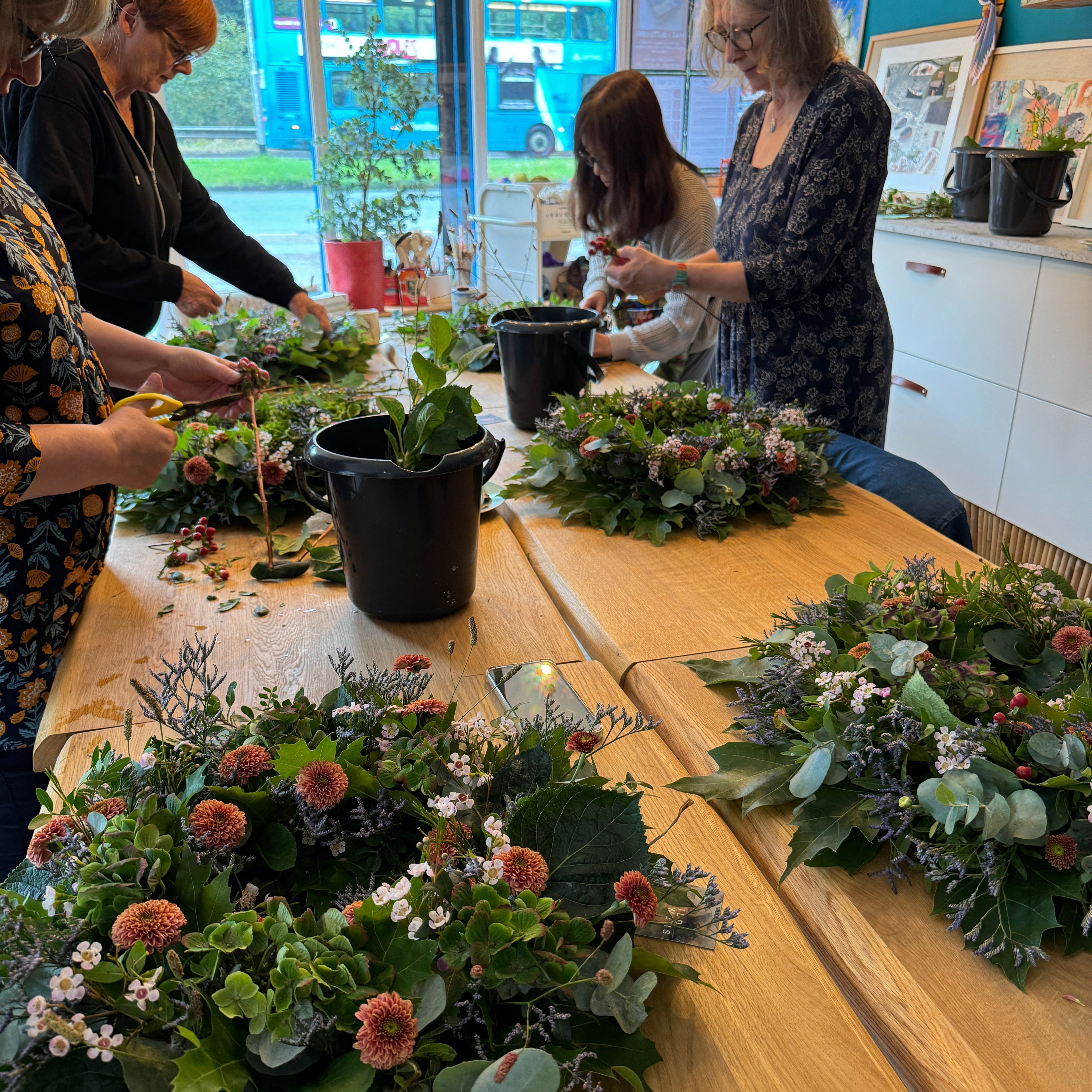 Two people working on floral arrangements in a bright room with large windows.