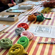 Colorful knitted items displayed on a striped wall with people in the foreground.