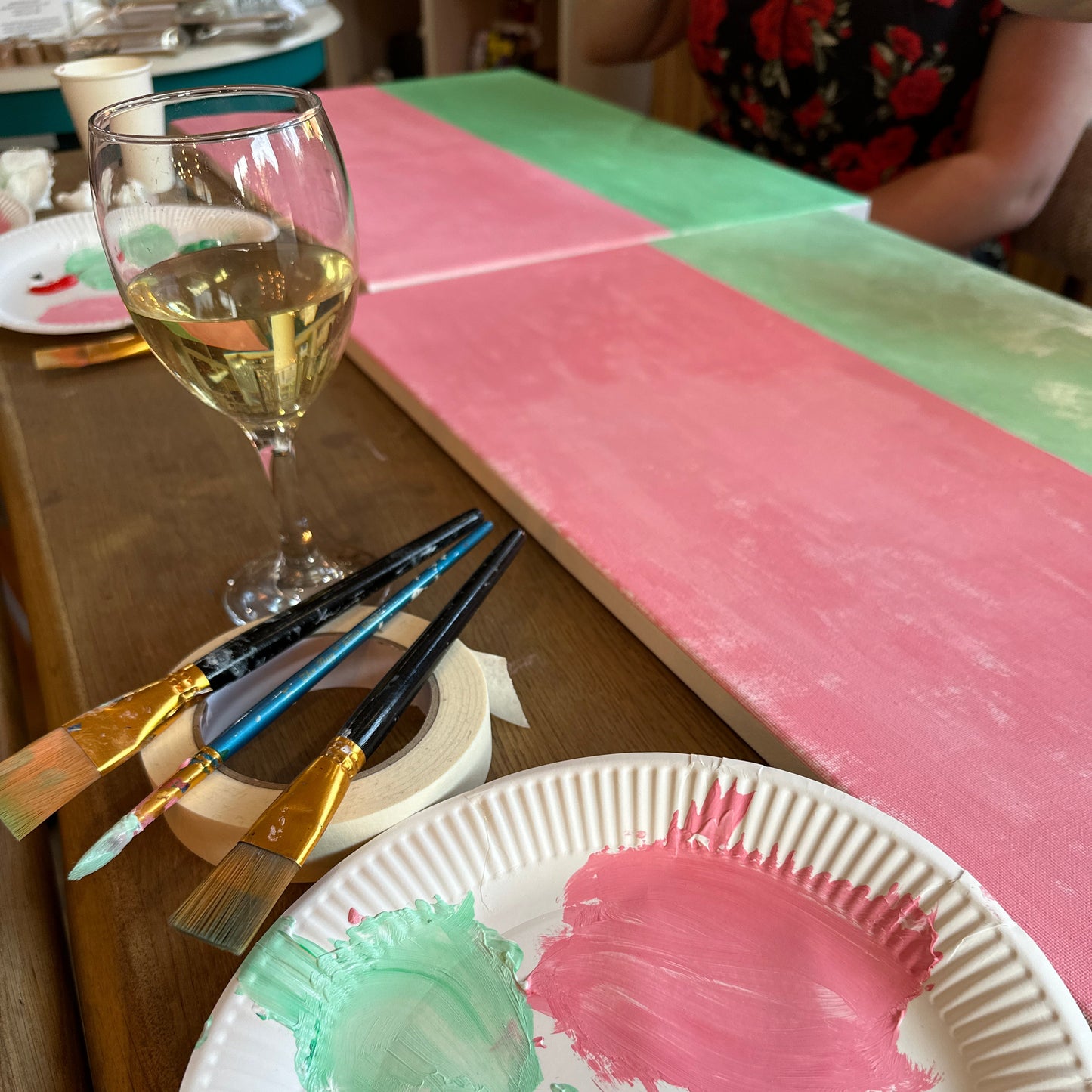Art supplies including paintbrushes and a paper plate with paint on a wooden surface.