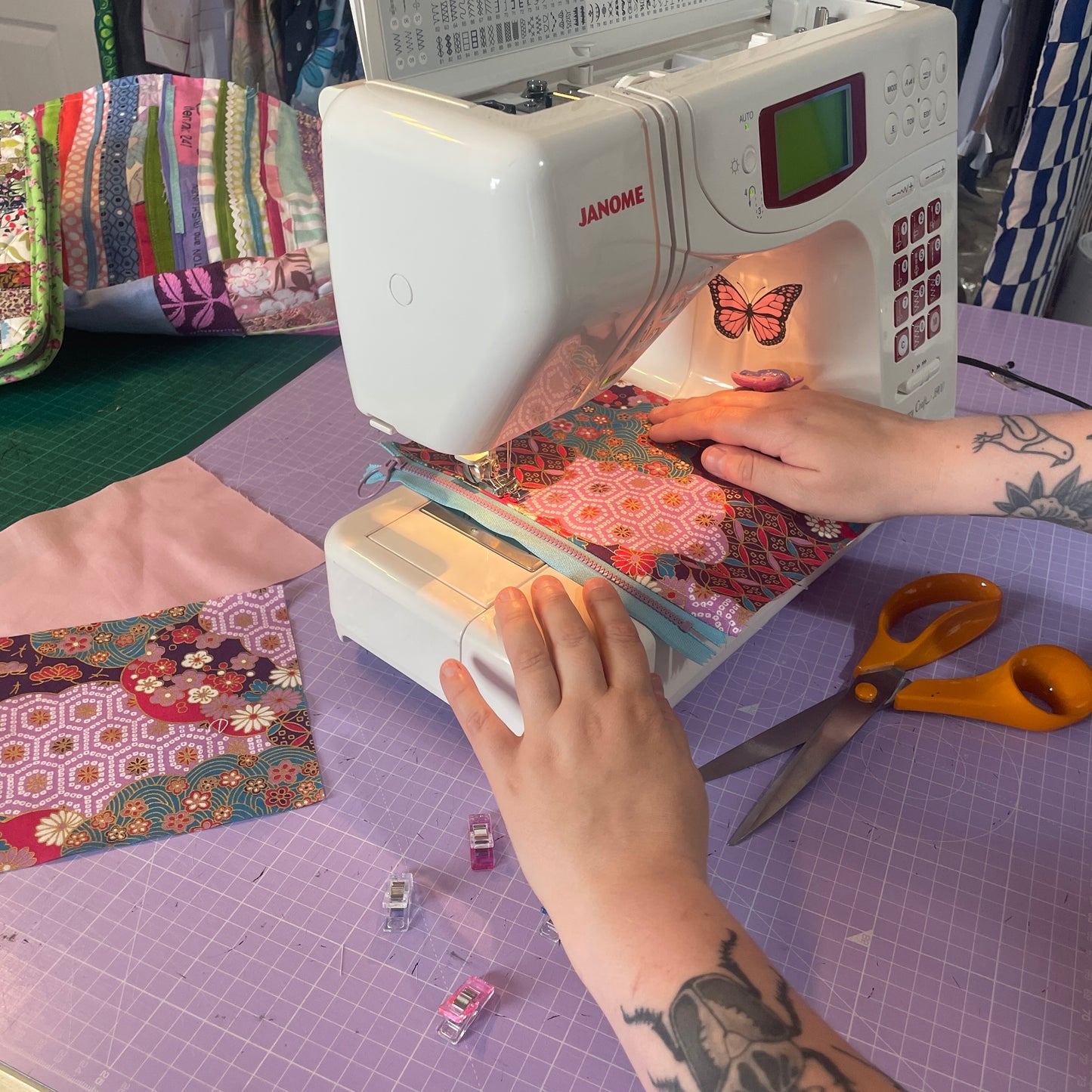 Person using a Janome sewing machine on a quilt with colorful fabric pieces.