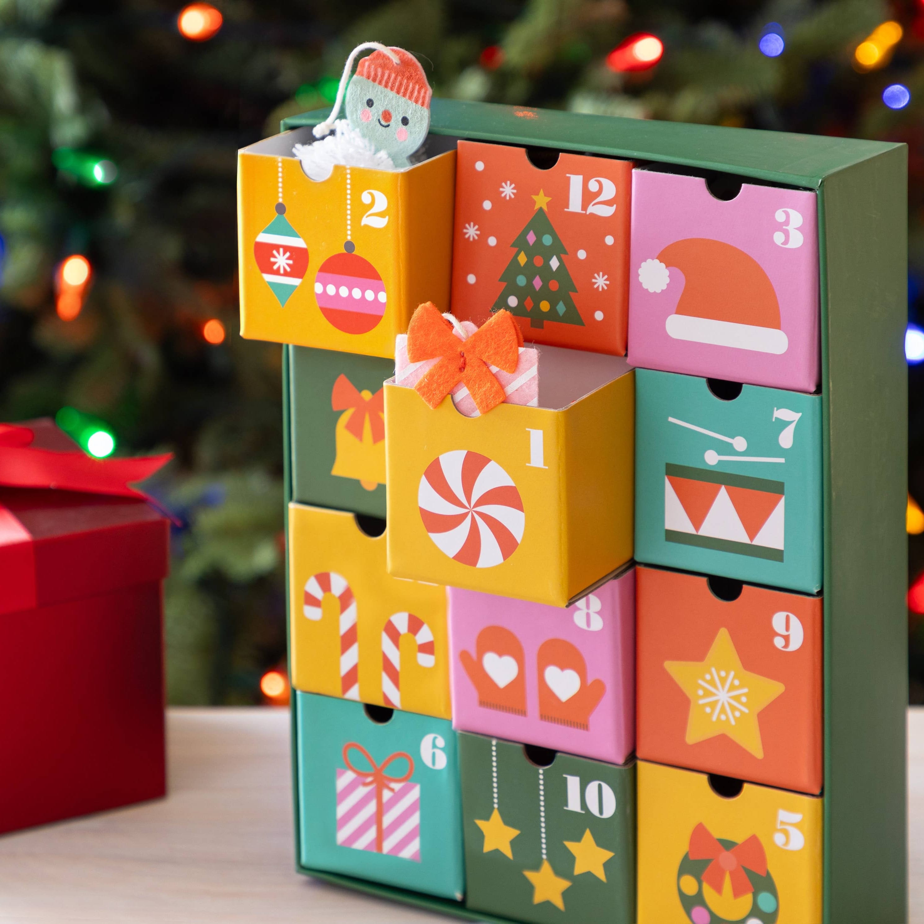 Colorful advent calendar with numbered drawers in front of a Christmas tree.