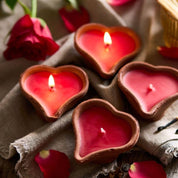 Heart-shaped candles on a textured fabric background with red roses and petals.