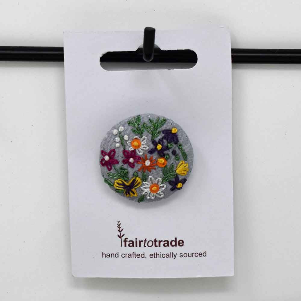Floral brooch on a 'fair to trade' branded card against a white background