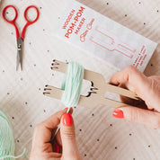 Person making pom-poms with yarn and tools on a polka dot surface
