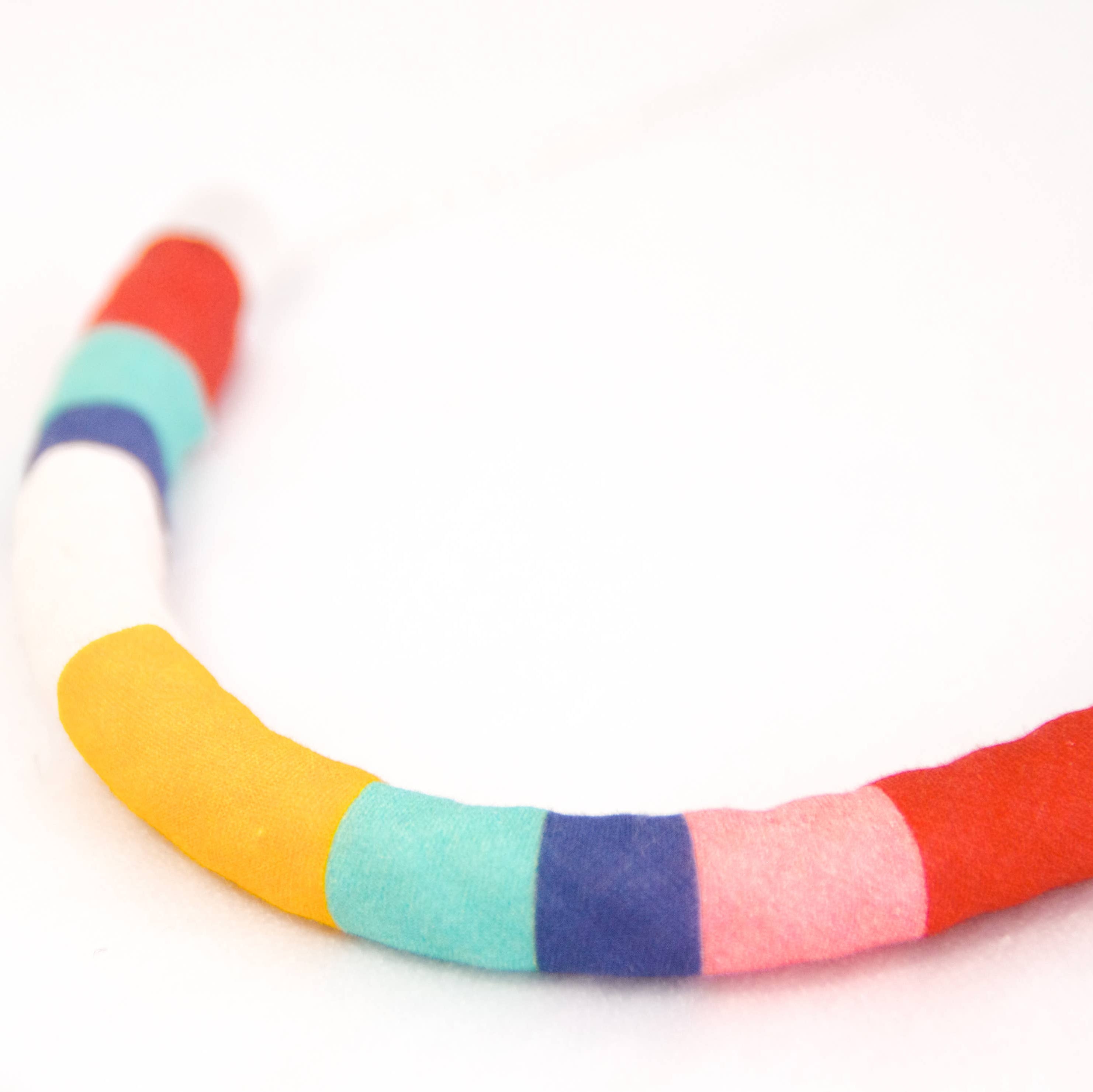 A curved foam headband with alternating colorful stripes of red, white, blue, yellow, mint green, navy, pink, and red on a plain white background.