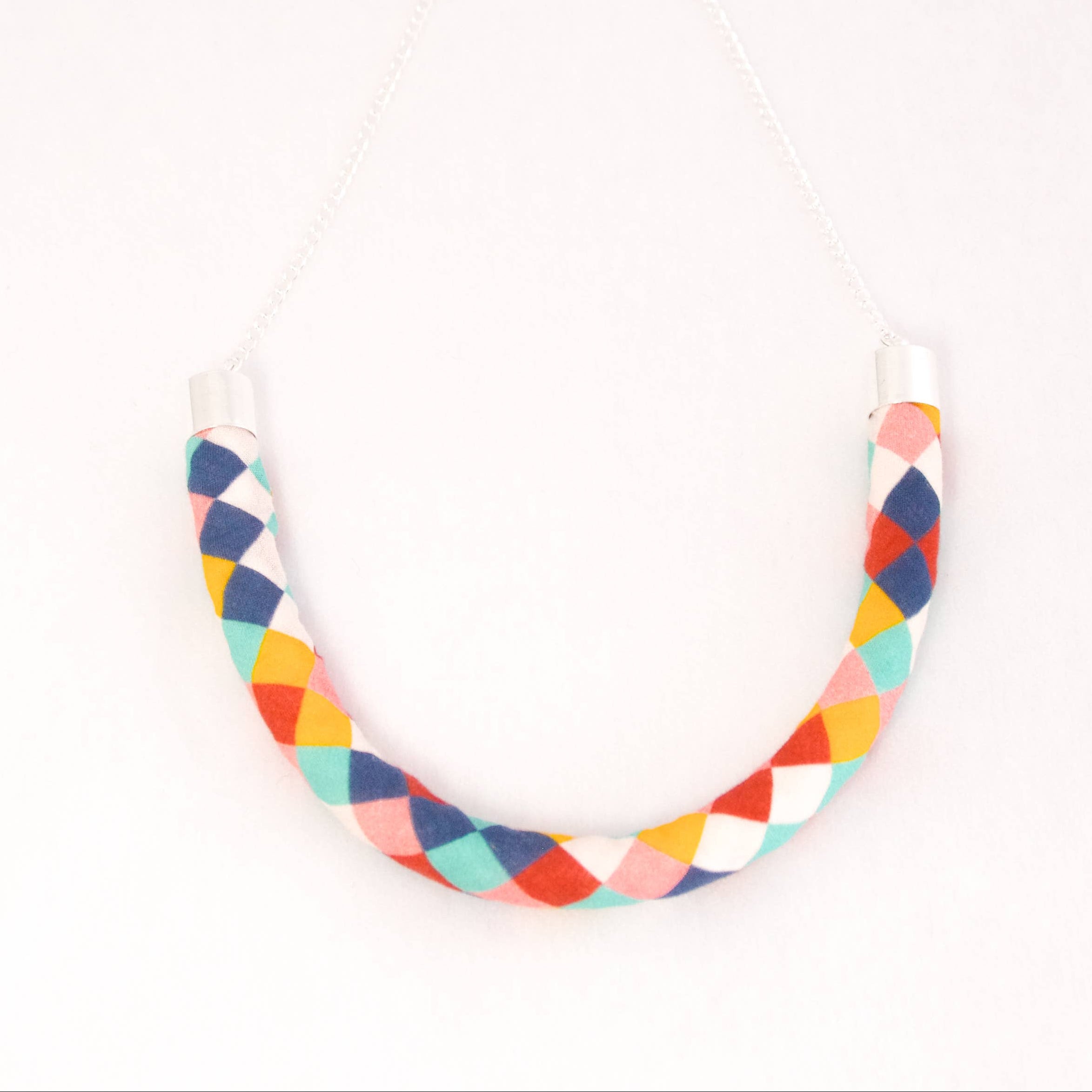 A U-shaped necklace featuring a colorful geometric pattern of interlocking diamond shapes in navy, orange, red, yellow, and white, suspended on a thin silver-toned chain against a plain white background.