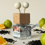 A reed diffuser bottle with a wooden cap and two white reed tips, surrounded by tea leaves, limes, and orange slices on a light beige background. The label reads 'THE EARL GREY BLANC TEA HERBAND CITRUS'.