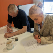 Two people sitting at a table with papers and pens, engaged in an activity.