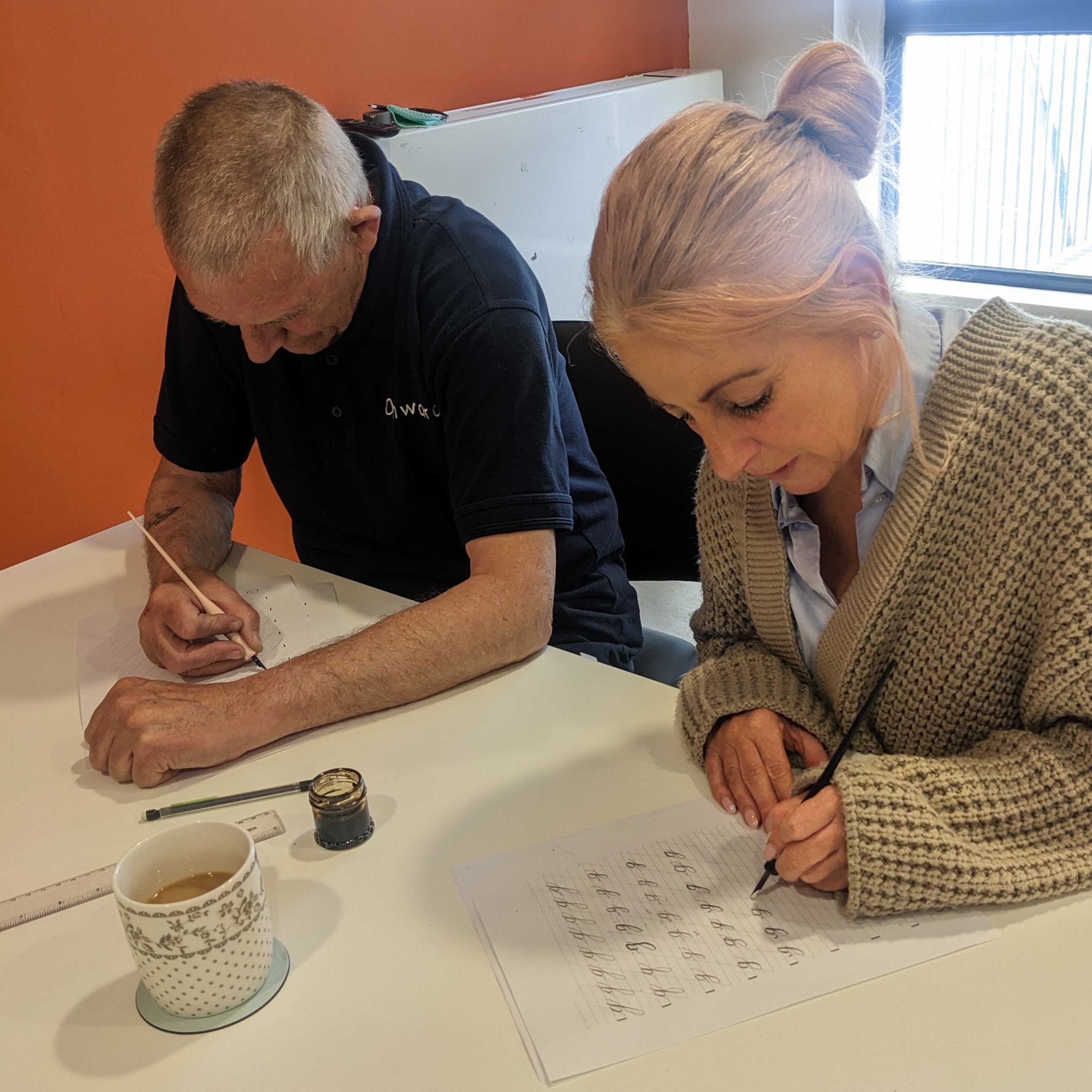 Two people sitting at a table with papers and pens, engaged in an activity.