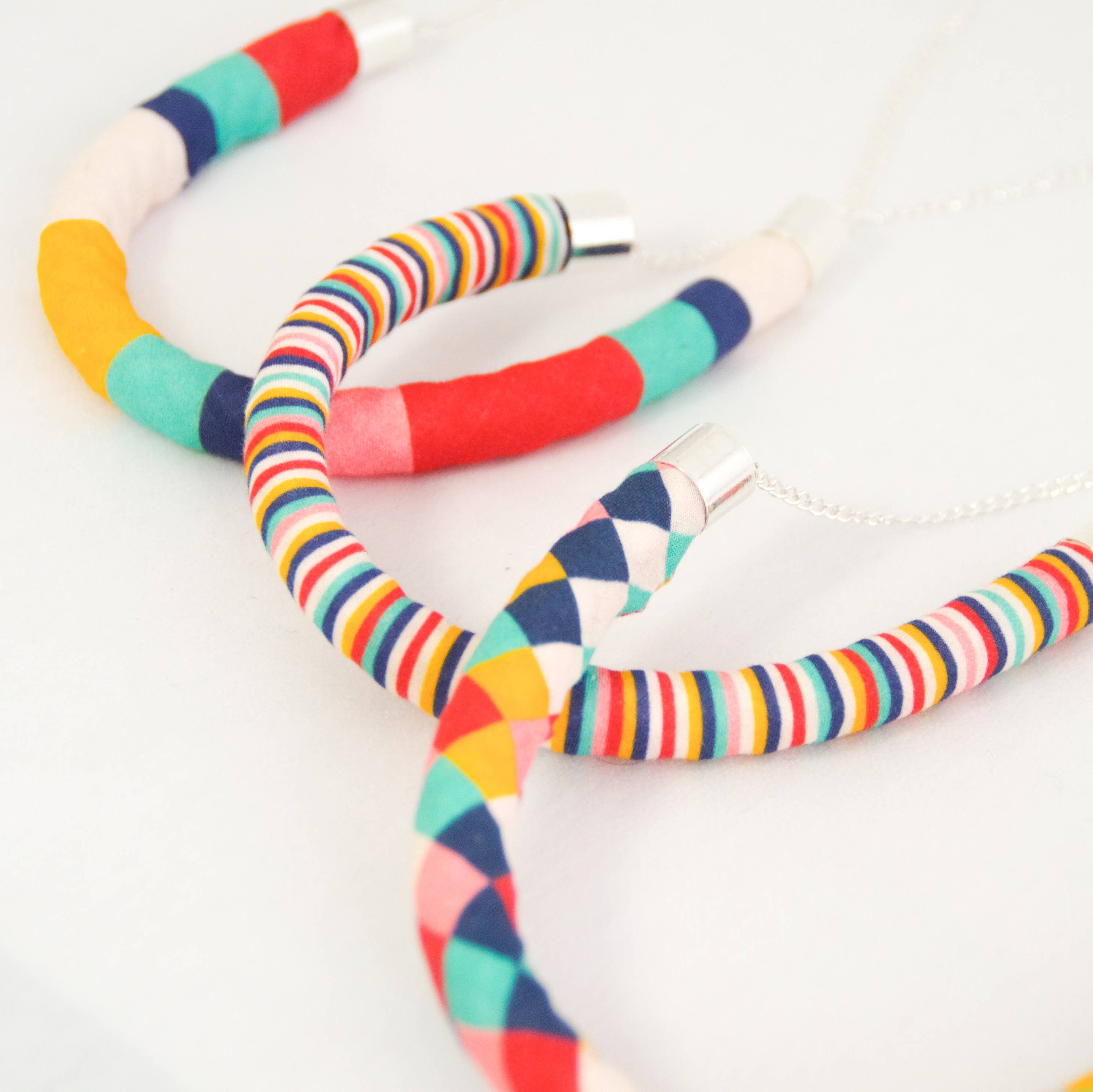 Three colorful fabric-covered hoop necklaces with silver-toned metal caps and chains, arranged on a plain white background.