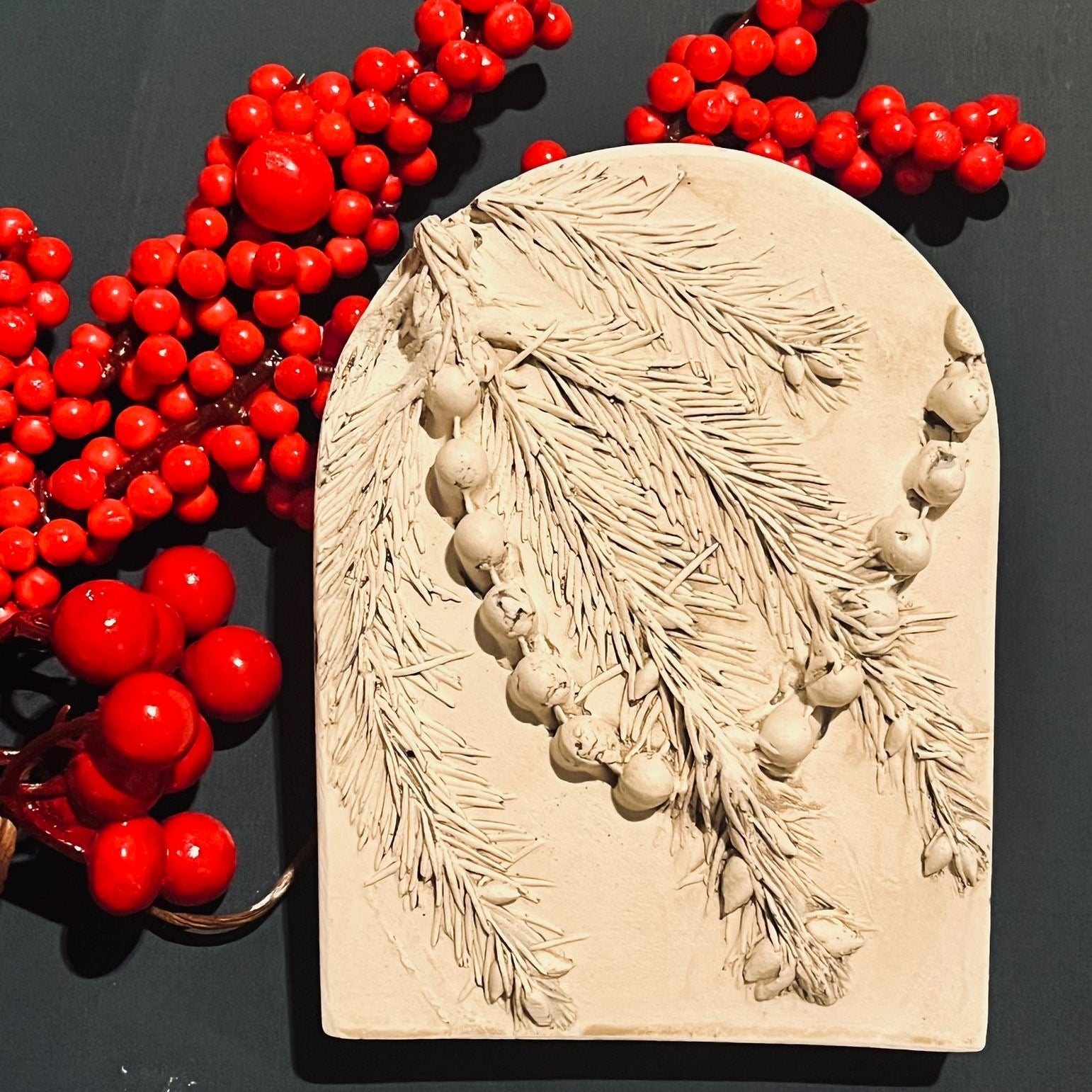 Decorative stone with leaf and berry design next to red berries on a dark background