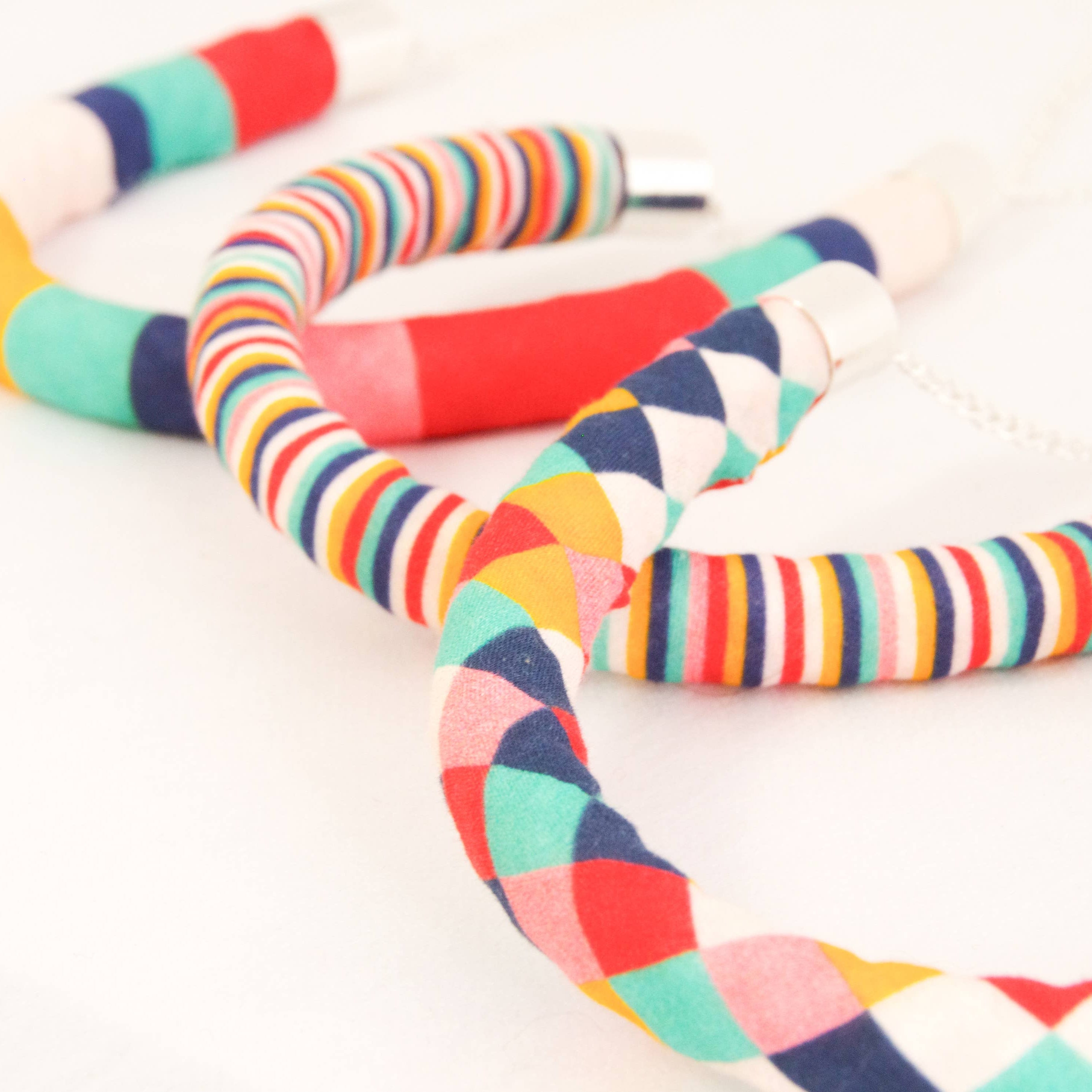 Three colorful striped fabric necklaces with silver metal connectors, arranged on a clean white background.