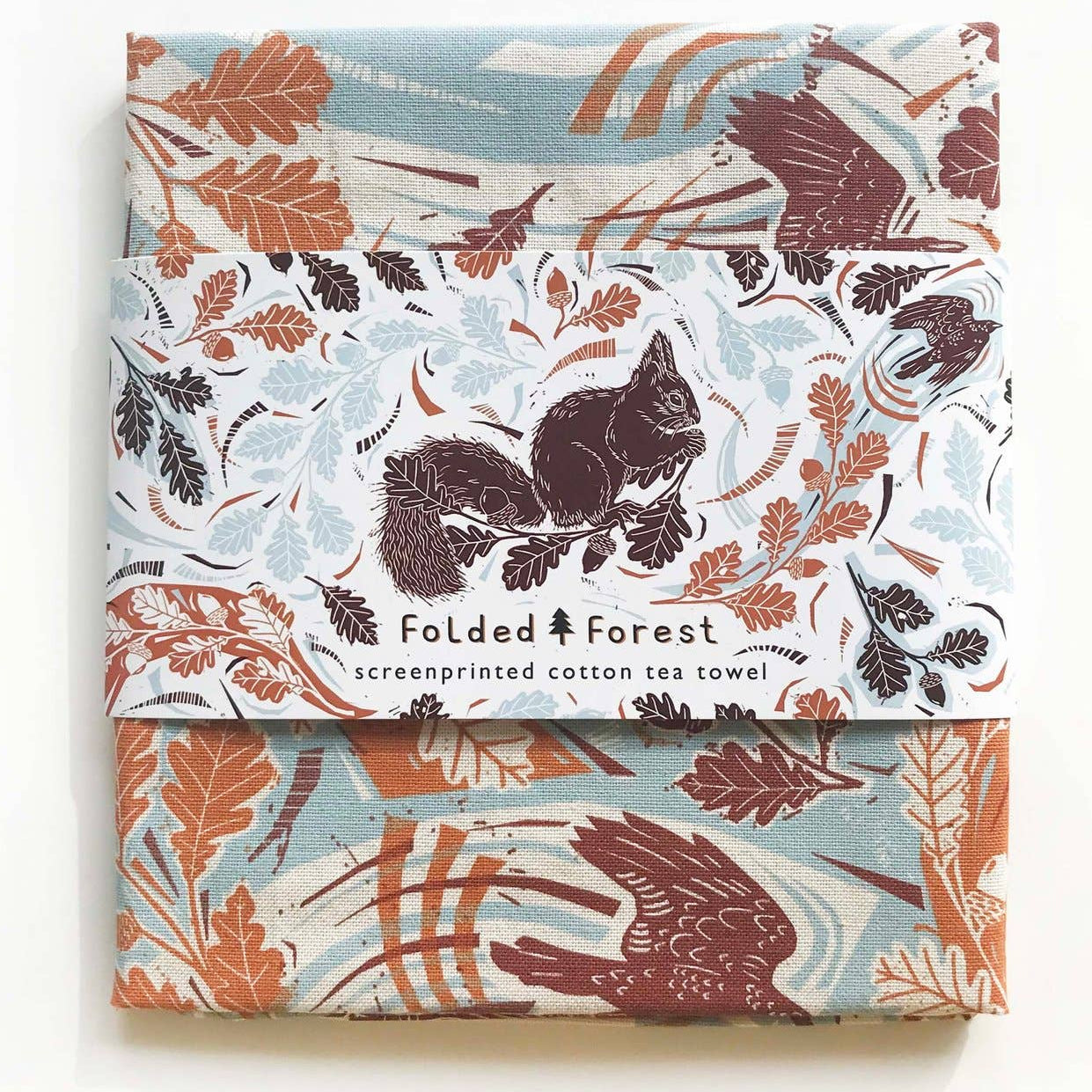 Packaged cotton tea towels with forest-themed design on a white background
