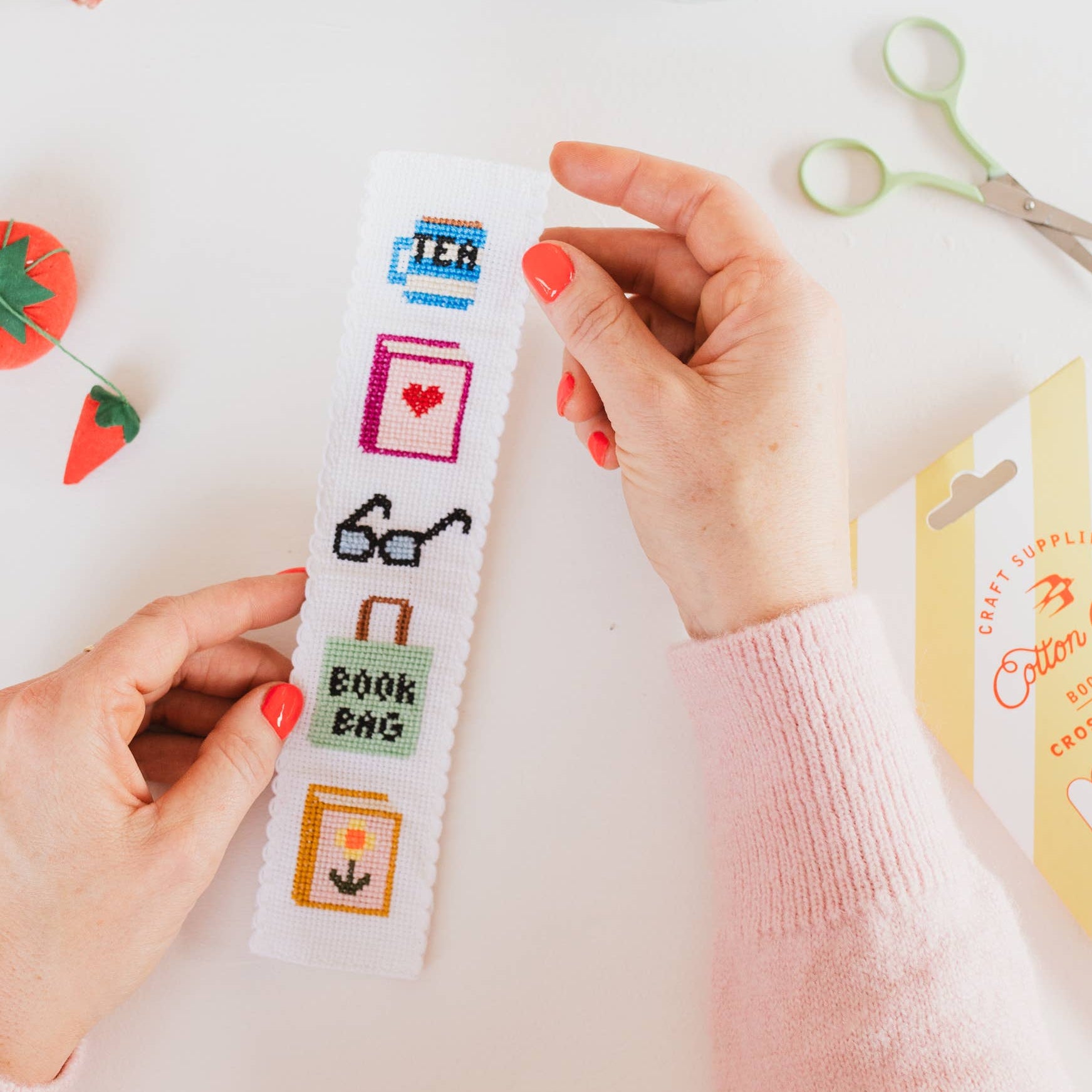 Person holding a colorful bookmark with icons on a desk with stationery items.