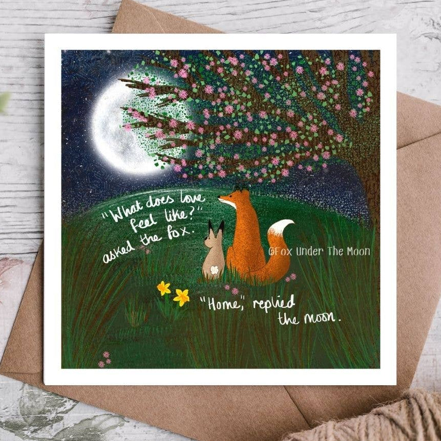 Greeting card with fox and rabbit illustration under a moonlit tree, on a wooden surface.