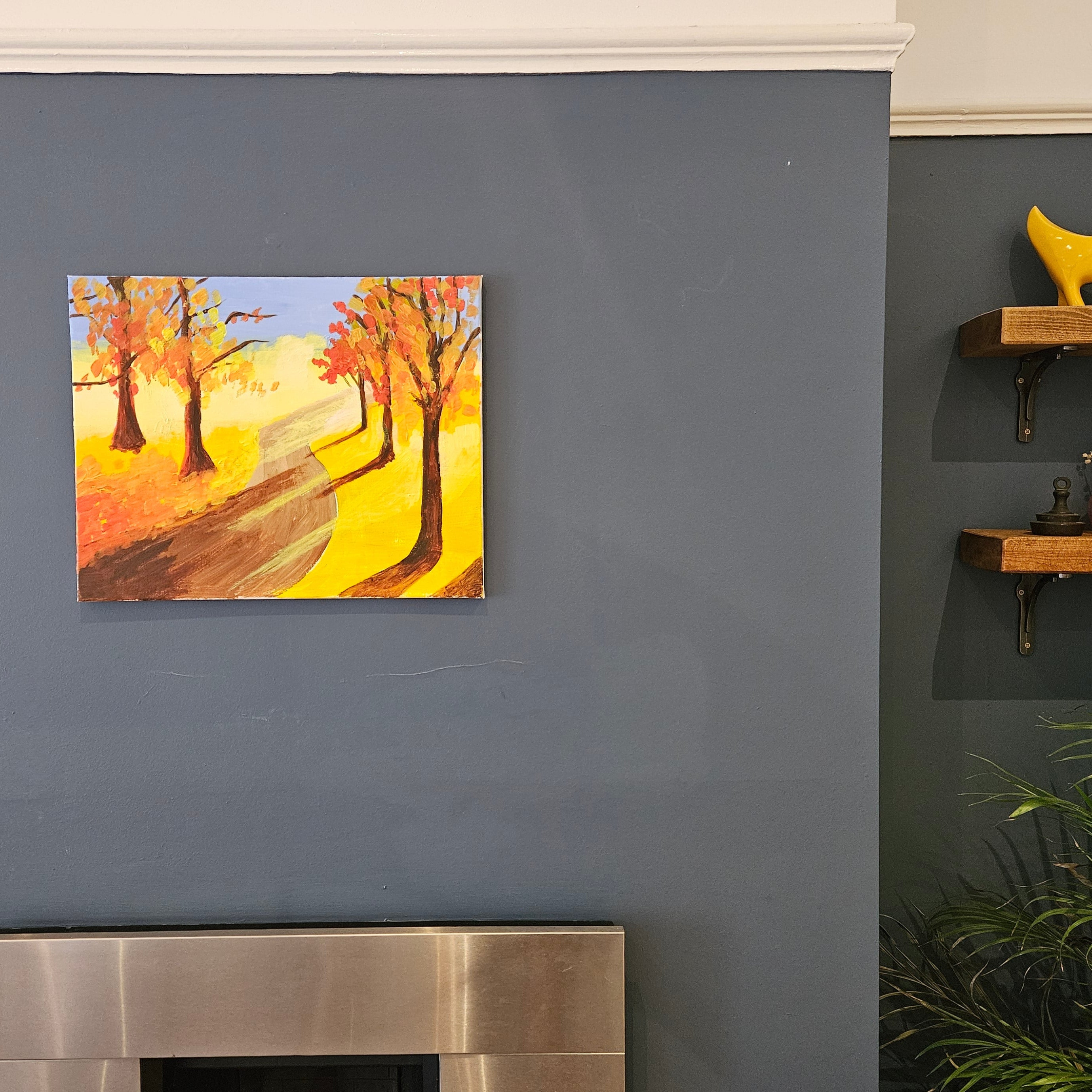 Painting of a autumn landscape on a gray wall above a fireplace.