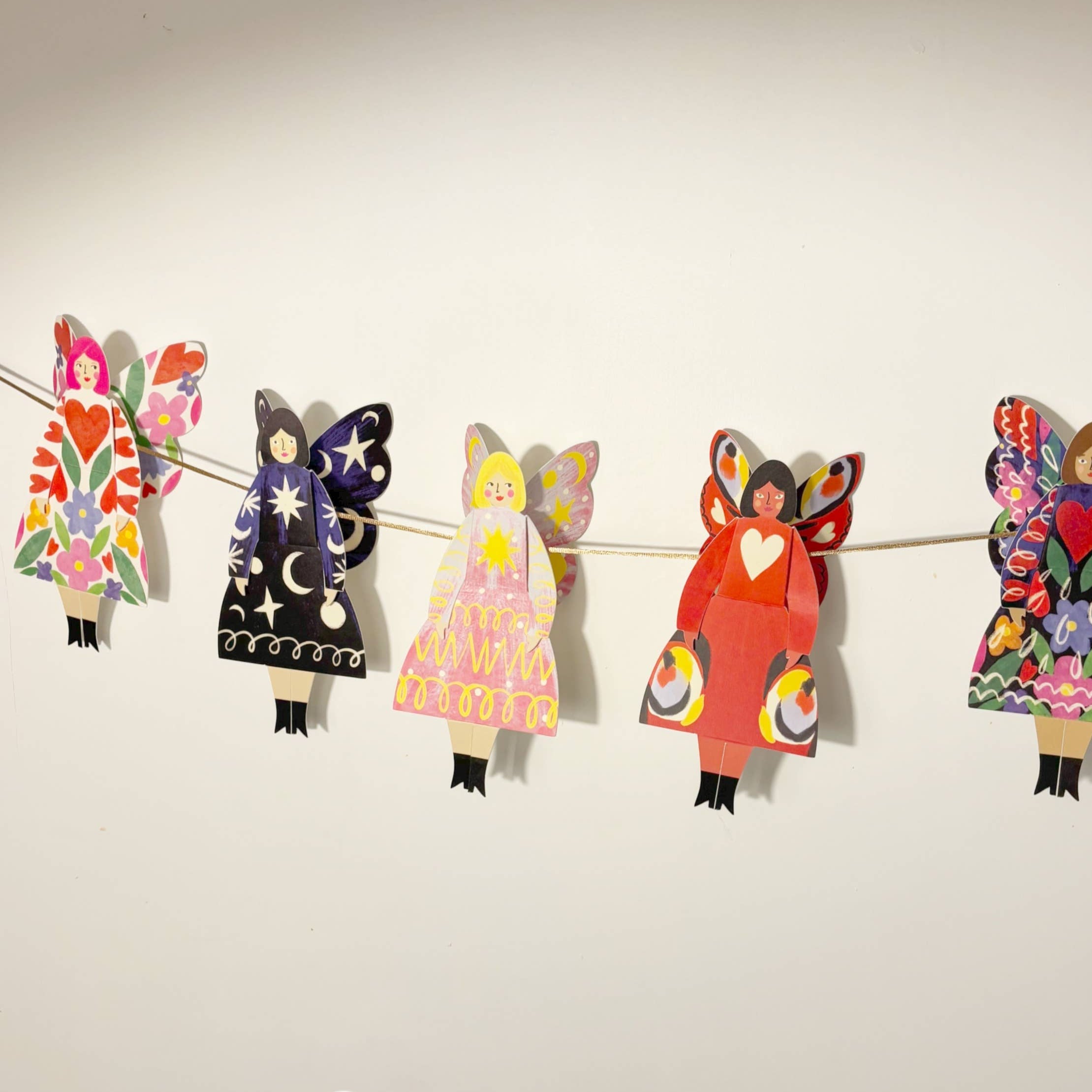 Colorful paper dolls of 'Butterfly Women' by Kitty Kenda hanging on a string against a plain background.