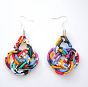 A pair of handmade teardrop-shaped dangle earrings made from colorful patterned fabric strips knotted into a knot, hanging from silver fishhook wires on a plain white background.