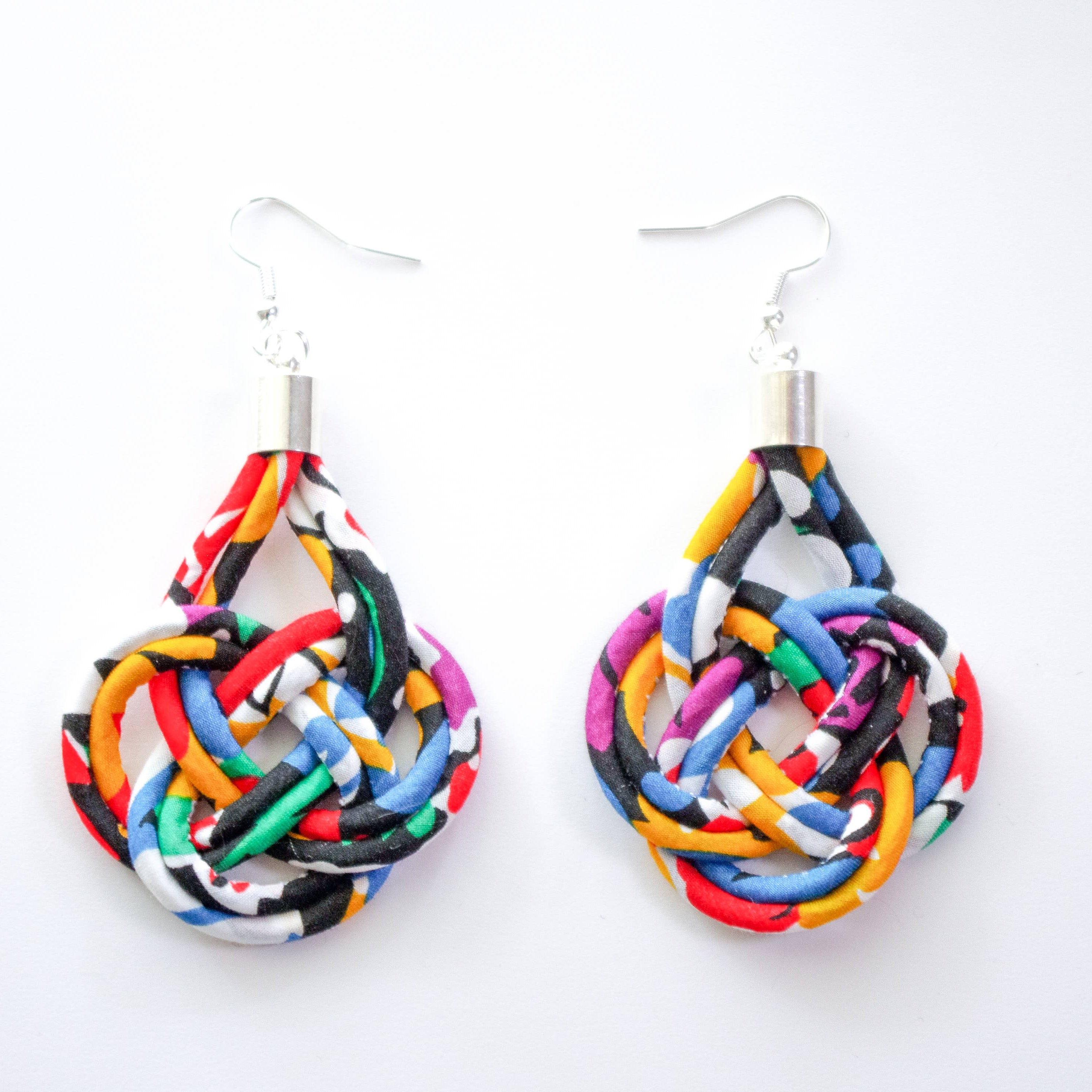 A pair of handmade teardrop-shaped dangle earrings made from colorful patterned fabric strips knotted into a knot, hanging from silver fishhook wires on a plain white background.