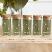 Five green jars with cork lids labeled 'ellis grey' on a wooden surface.
