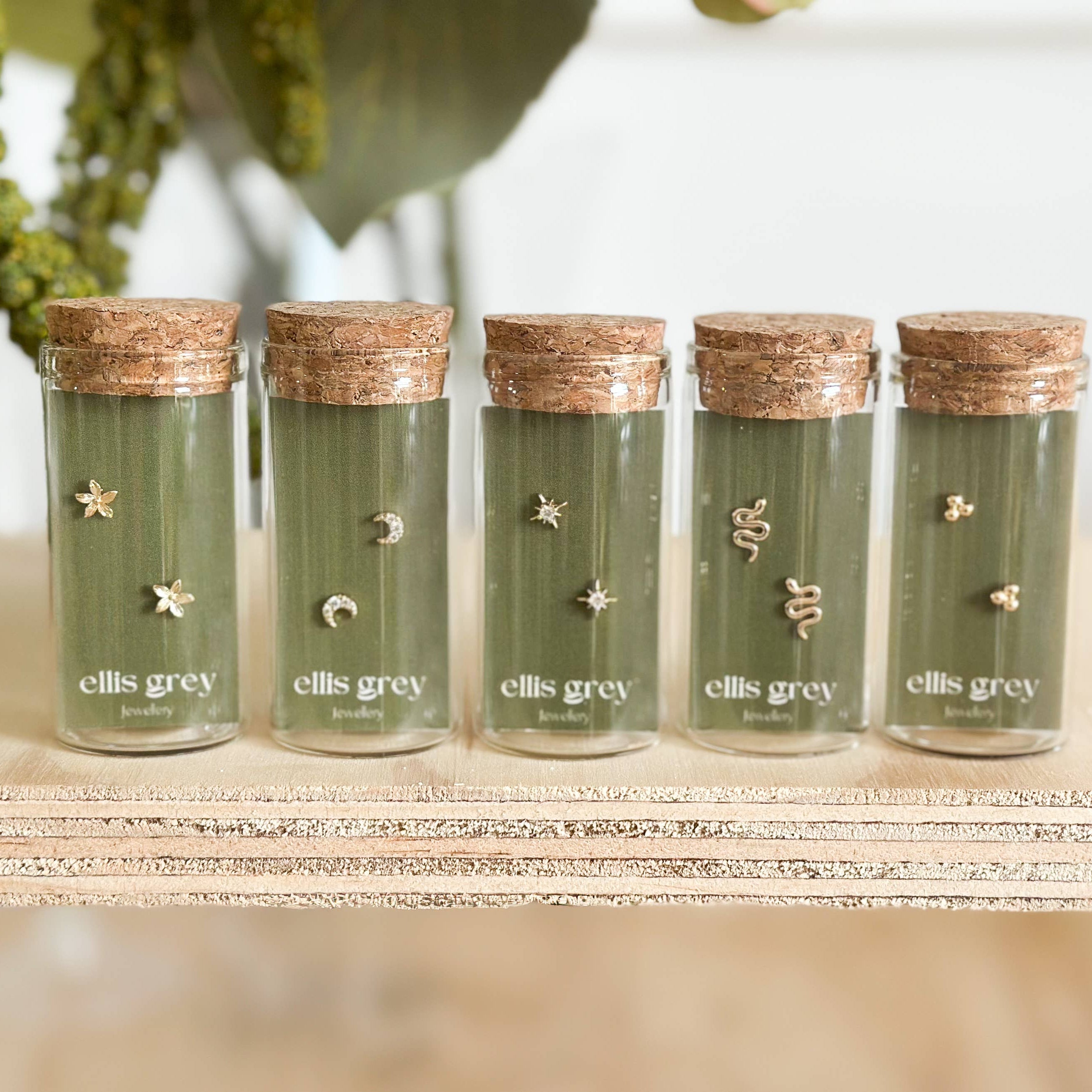 Five green jars with cork lids labeled 'ellis grey' on a wooden surface.
