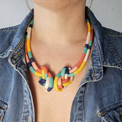 A close-up of a person wearing a colorful braided rope necklace with a knot design, styled with a blue denim jacket.