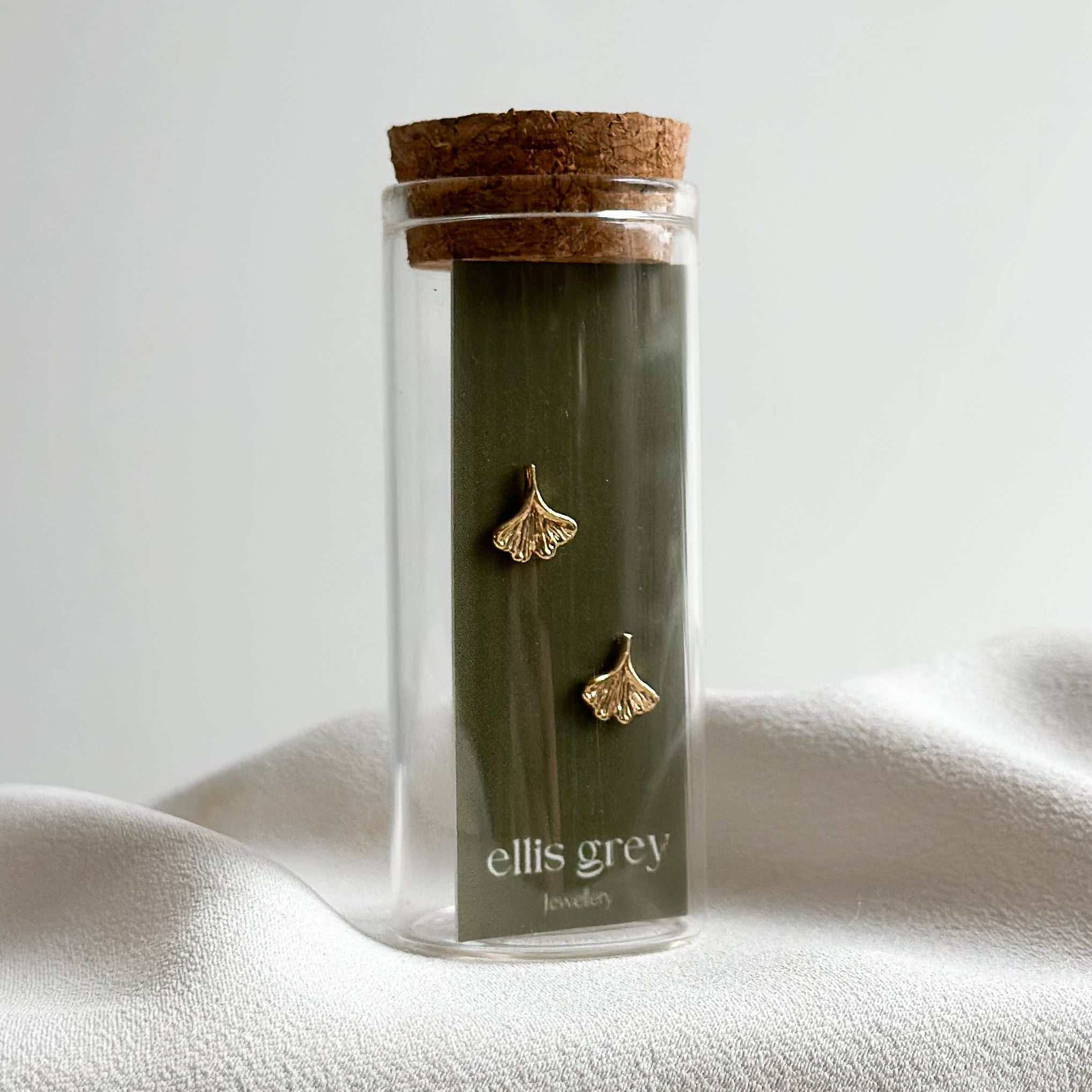 Glass jar with cork lid containing gold earrings on a white surface