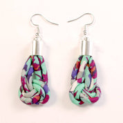 A pair of handmade dangle earrings featuring knotted fabric tassels with a colorful floral pattern in pink, purple, green, and white, suspended from silver fishhook wires on a plain white background.
