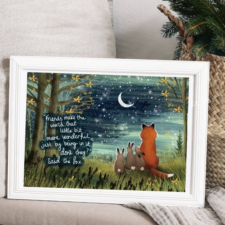 Framed artwork with fox and rabbits under a starry night sky, placed on a surface.