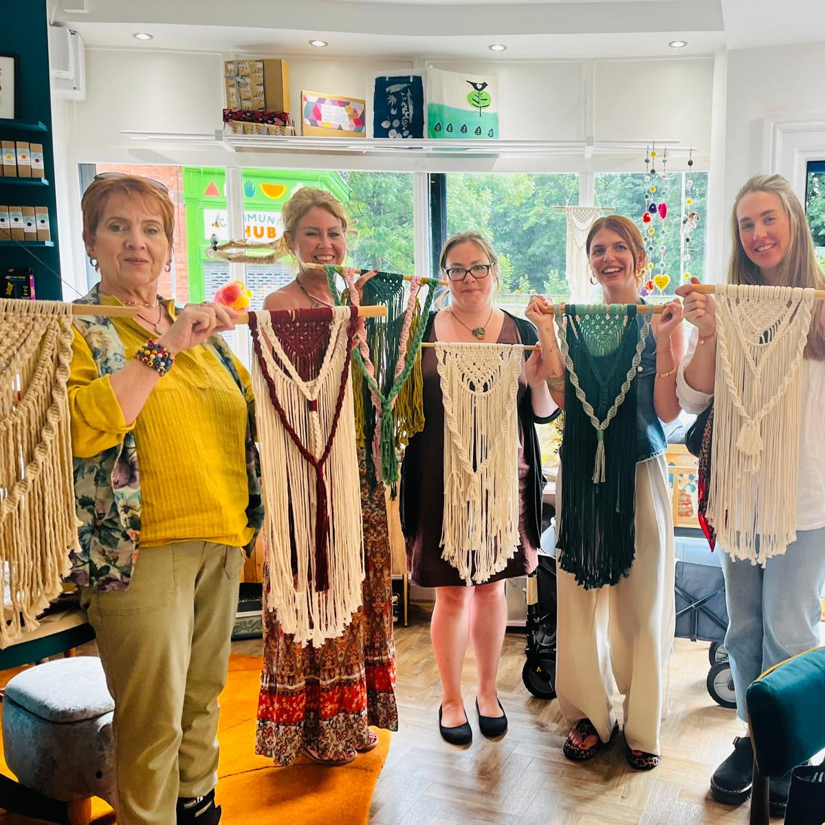 Group of people holding up handmade lace garments in a room with large windows.