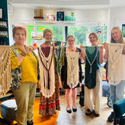 Group of people holding up handmade lace garments in a room with large windows.