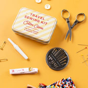 Travel sewing kit with tin, scissors, thread, pins, and other supplies on a yellow background