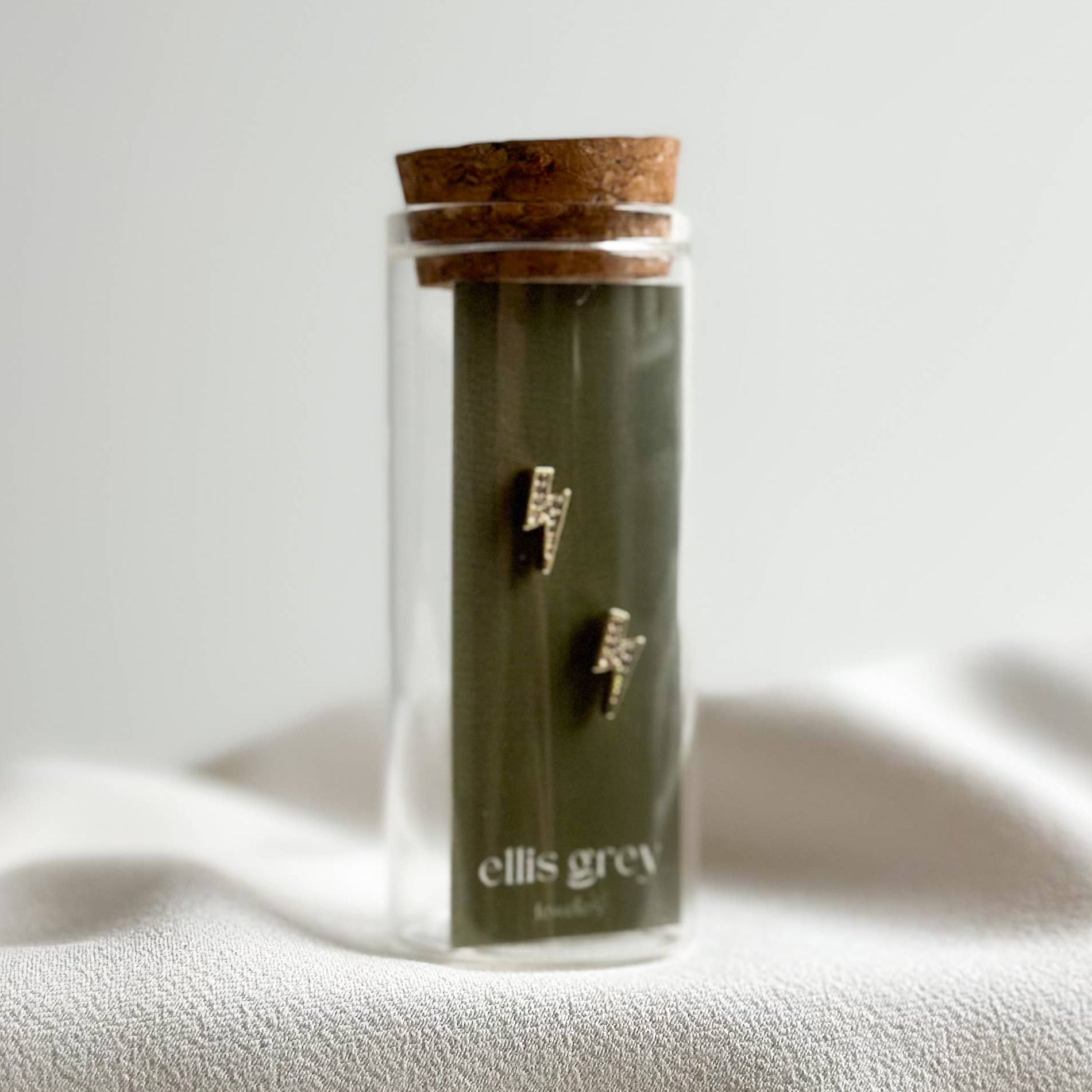 Glass jar with cork lid containing jewelry on a white fabric background