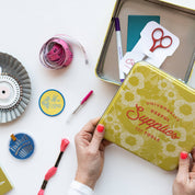 Person holding a yellow tin labeled 'Supplies' with stationery items on a white background