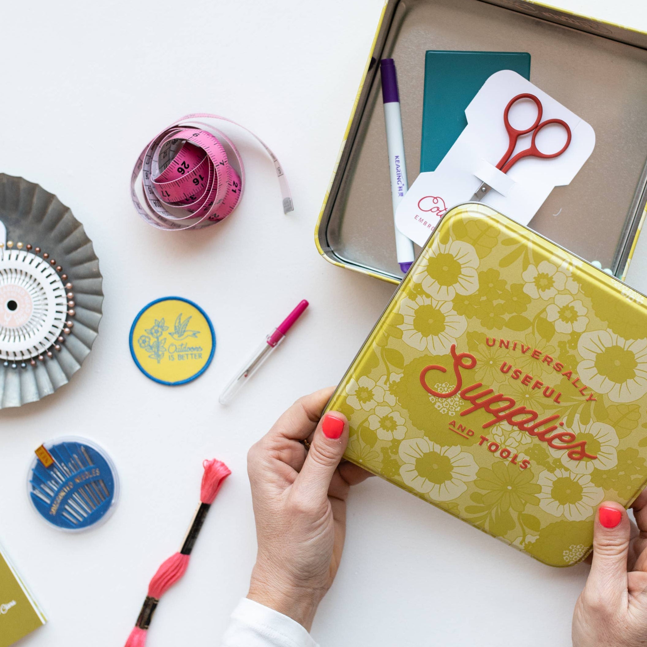 Person holding a yellow tin labeled 'Supplies' with stationery items on a white background