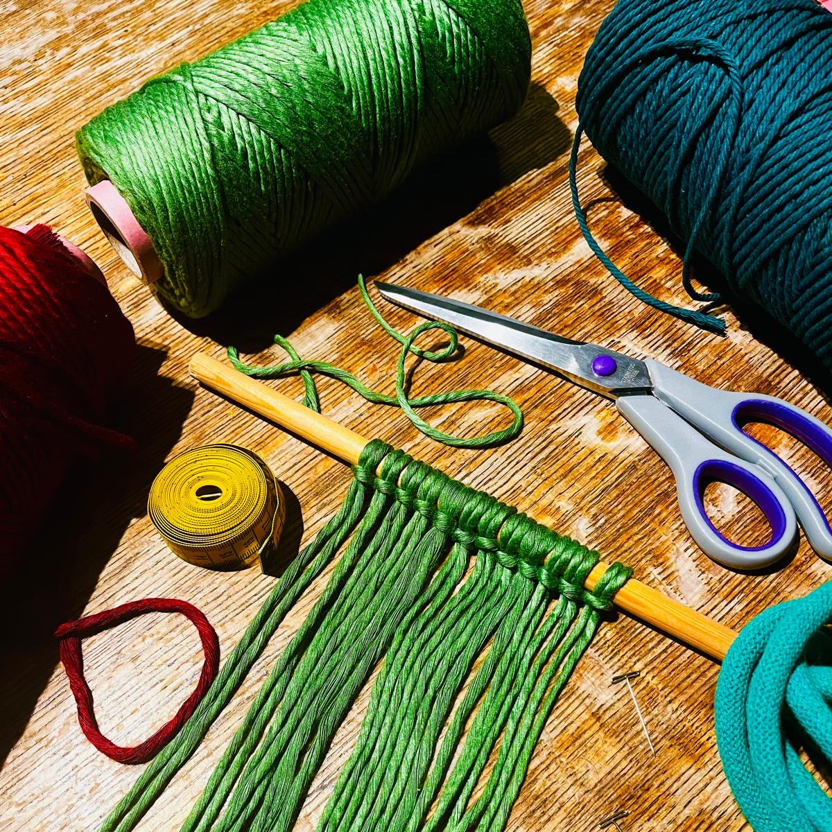 Green yarn with a partially completed craft project on a wooden surface, with scissors and other yarns in the background.