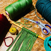 Green yarn with a partially completed craft project on a wooden surface, with scissors and other yarns in the background.