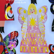 Colorful paper cutout of a butterfly woman with a pink dress and yellow accents, surrounded by other decorative elements.