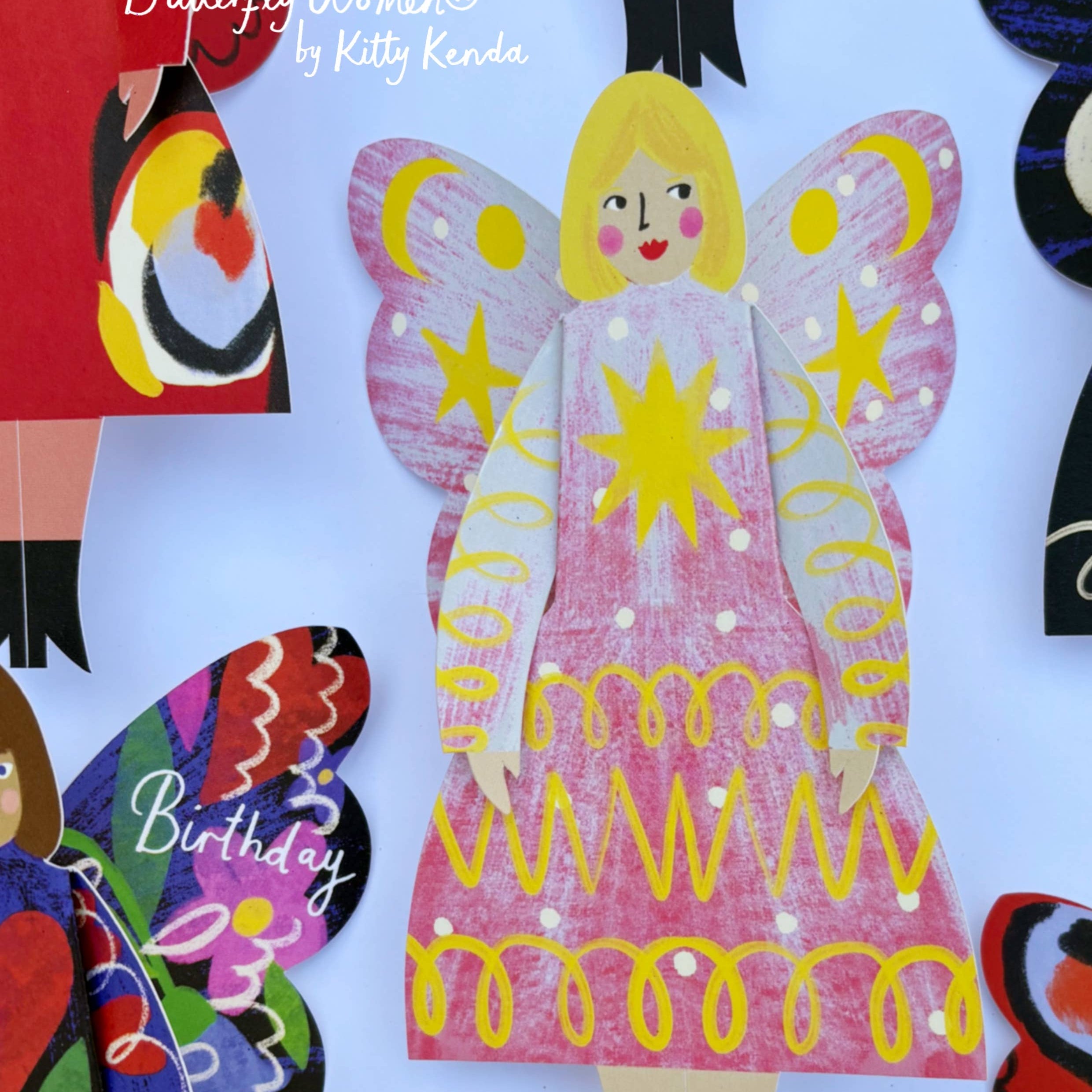 Colorful paper cutout of a butterfly woman with a pink dress and yellow accents, surrounded by other decorative elements.