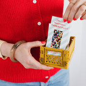 Person holding a yellow crate with thread packets, wearing a red sweater.