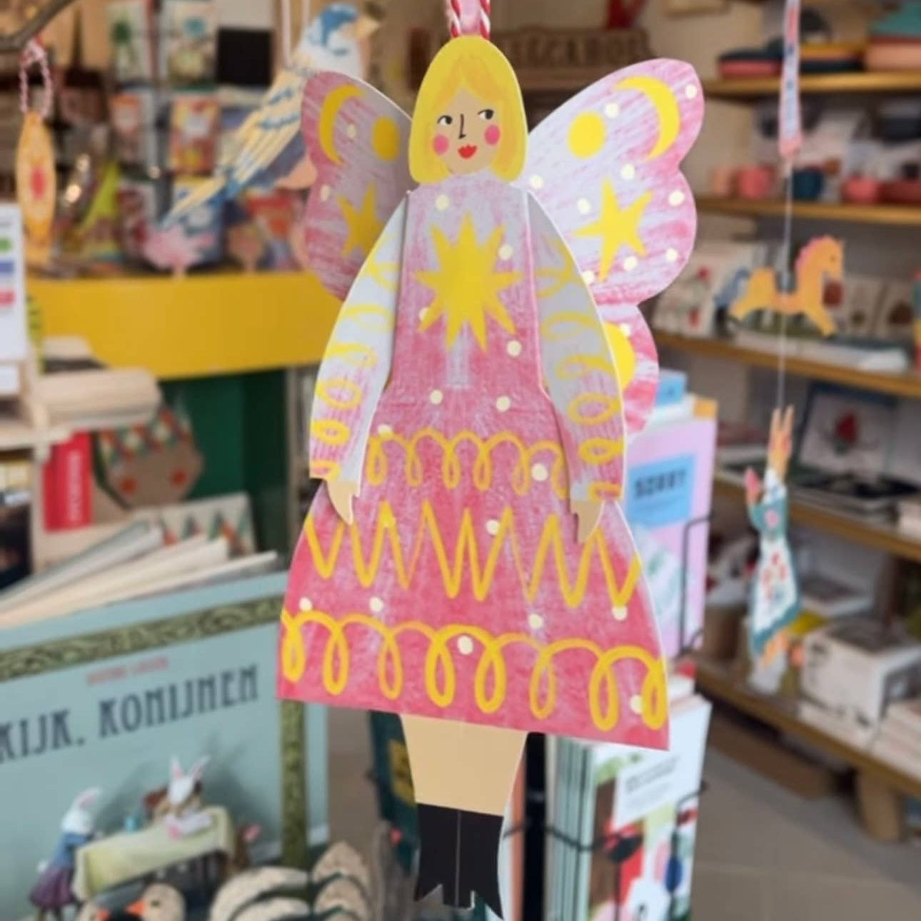 Decorative angel figure with pink dress and yellow hair hanging in a store.