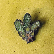 A round handmade ceramic plate in a textured olive-green glaze, styled in a flat-lay arrangement with a small green leaf in the center, a white succulent, and a small seashell on a gray background.