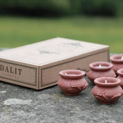 Set of small pink ceramic pots with candles next to a 'DALIT' branded box on a stone surface.