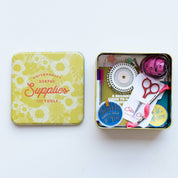 Open tin box with various tools and a colorful lid on a white background