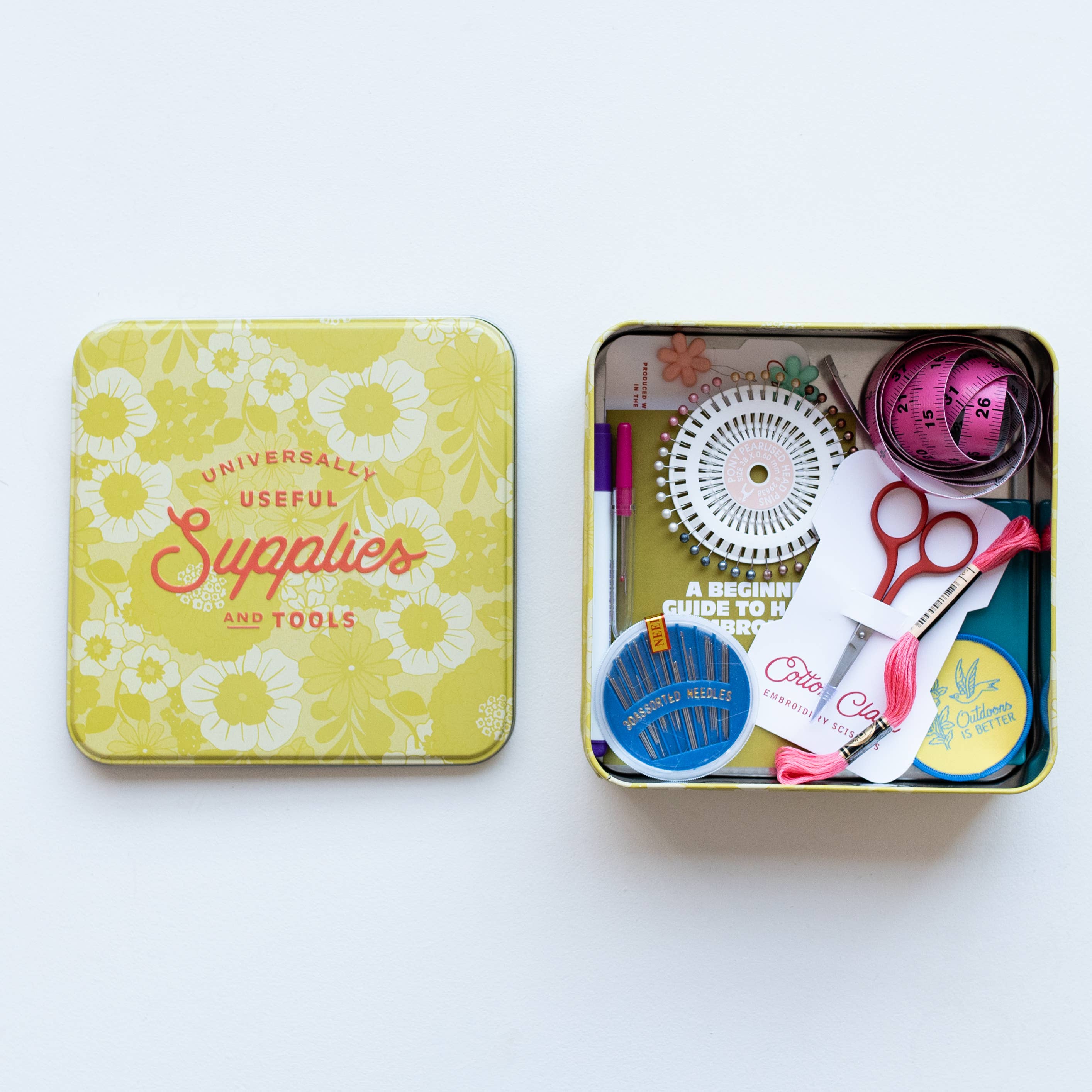 Open tin box with various tools and a colorful lid on a white background